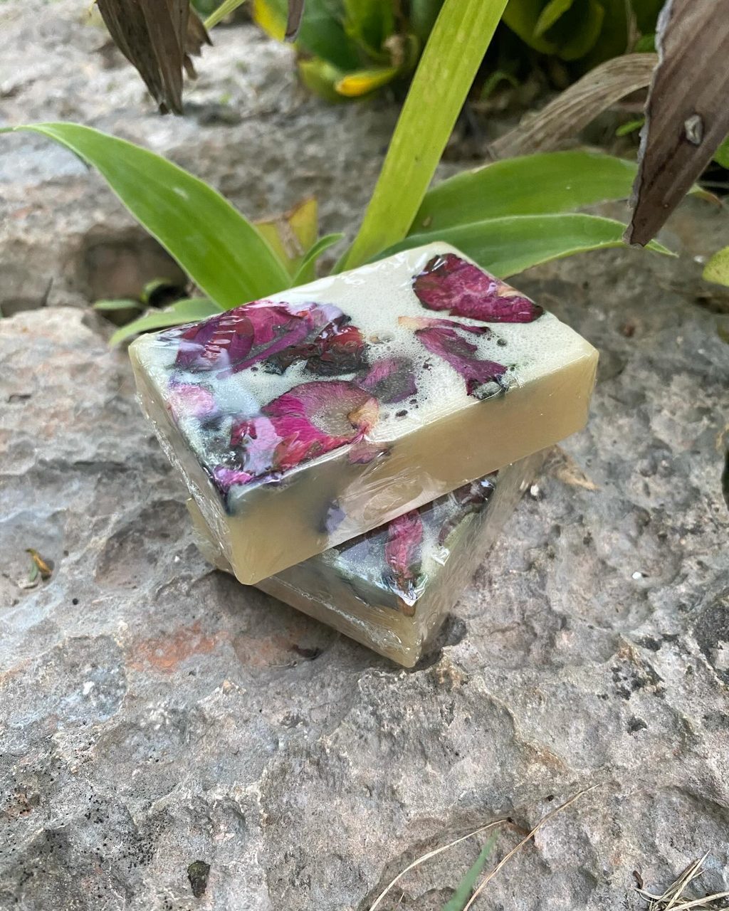Handmade soap with pressed rose petals resting on stone